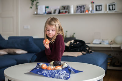 Girl looking at easter egg while sitting on table at home