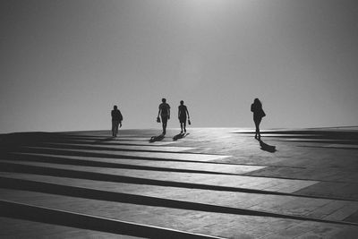 Silhouette people walking against clear sky during sunny day