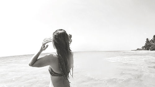 Rear view of woman standing at beach against sky