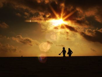 Silhouette people walking at beach against sky during sunset