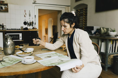 Female architect examining blueprint while working at home
