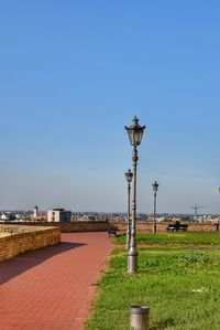 Street light by footpath against clear blue sky