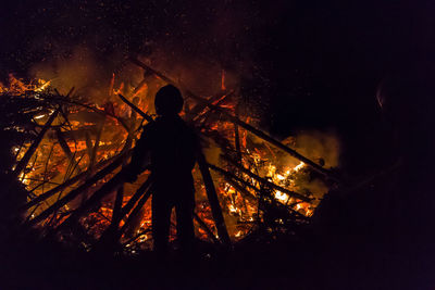 Rear view of silhouette person standing by burning woods at night