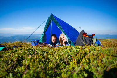 Group of people relaxing on field against blue sky