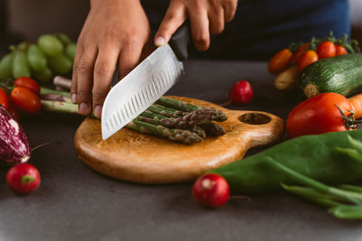 Hands chopping asparagus on wood chopping board preparing spring in kitchen with fresh vegetables