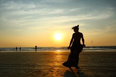 Silhouette woman standing at arambol beach against sky during sunset
