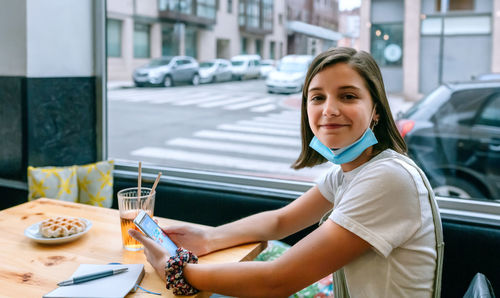 Young woman with removed mask smiling looking at camera in a coffee shop