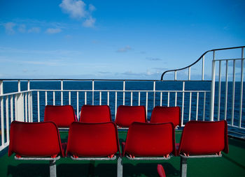 Empty chairs by sea against sky