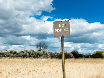 Information sign on field against sky