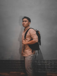 Young man looking away while standing against wall