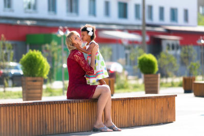 Daughter kissing mother while sitting on seat in city