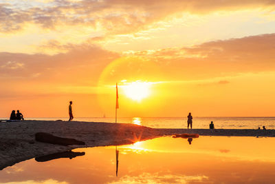 Silhouette people on beach against sky during sunset