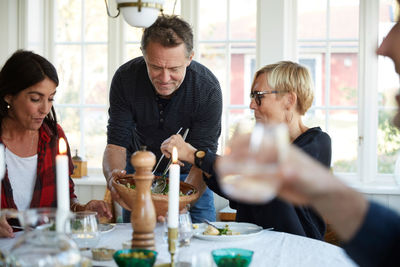 Mature man serving food to female friends at home