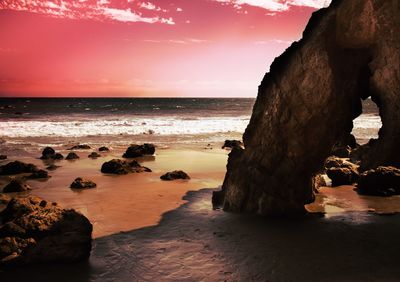 Rocks on beach against sky during sunset