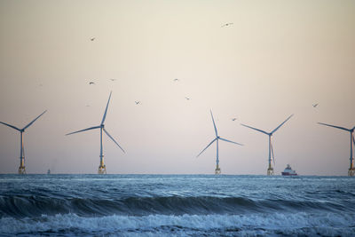 Wind turbines by sea against sky