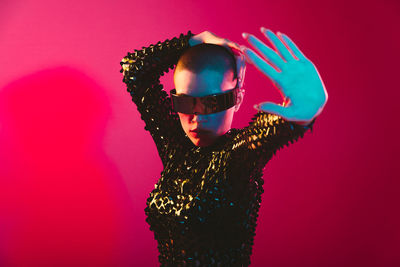 Woman wearing sunglasses standing against pink background