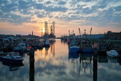 Boats moored in river against cloudy sky during sunset at harbor