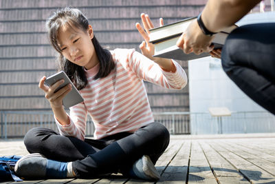 Young woman using mobile phone while sitting on laptop