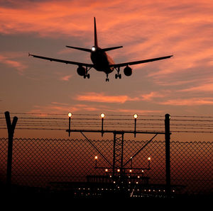 Low angle view of airplane flying above fence during sunset
