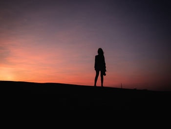 Silhouette woman standing on land against sky during sunset