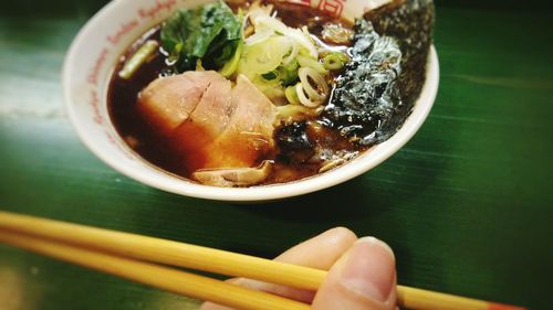 Cropped image of fingers holding chopsticks by food bowl