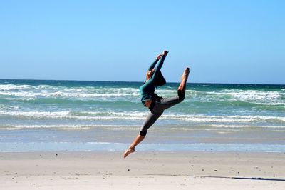 Ballerina practicing at beach against clear sky