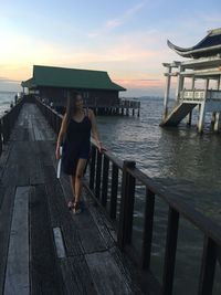 Full length of woman standing on pier by sea against sky during sunset