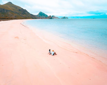 Friends sitting at beach against sky