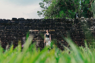 Full length of woman sitting against stone wall