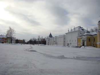 Snow covered road by buildings against sky
