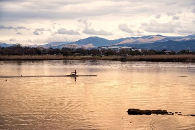 Man rowing on lake against cloudy sky during sunset