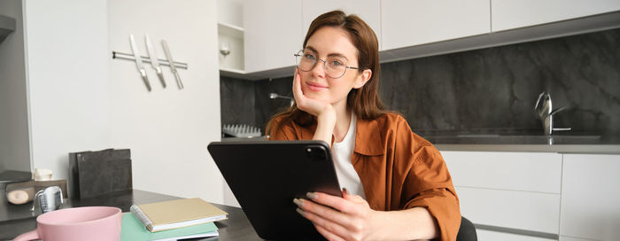 Young woman using digital tablet while sitting on table