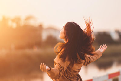 Woman standing at lakeshore against sky during sunset