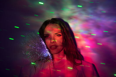 Portrait of beautiful young woman against illuminated background