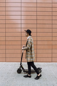 Man with umbrella walking on footpath against wall