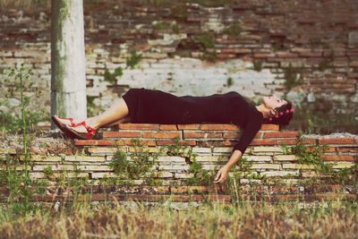 Side view of woman lying on retaining wall at park