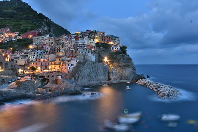 Illuminated buildings by sea against sky