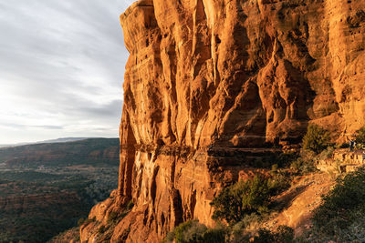 Person enjoys grand view at cathedral rock summit at sunset with golden hues.