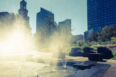 Fountain by buildings in city against sky