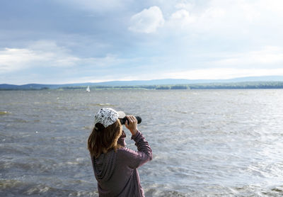 Rear view of woman standing by sea against sky