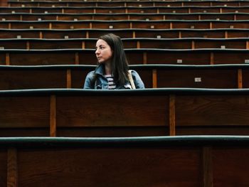 Young woman sitting amidst benches in lecture hall at university
