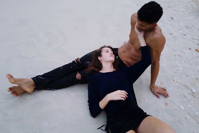 Interracial couple sitting at the beach on the sand touching each other