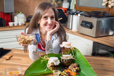 Portrait of smiling woman holding food at kitchen