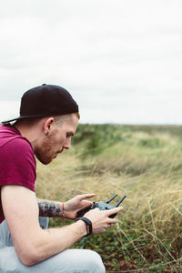 Side view of man using remote control while crouching on field against sky