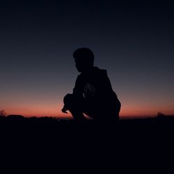 Silhouette man crouching against clear sky during sunset