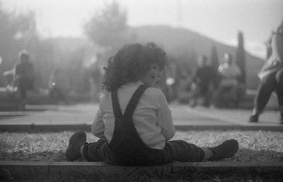 Rear view of boy sitting on street in city