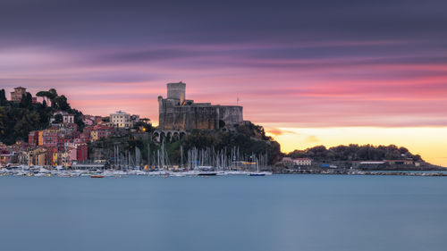 Buildings by sea against sky during sunset