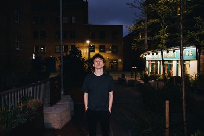 Portrait of young man standing against illuminated building at night