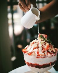 Cropped hand pouring milk on dessert