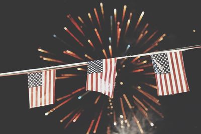 Low angle view of american flags against firework display at night